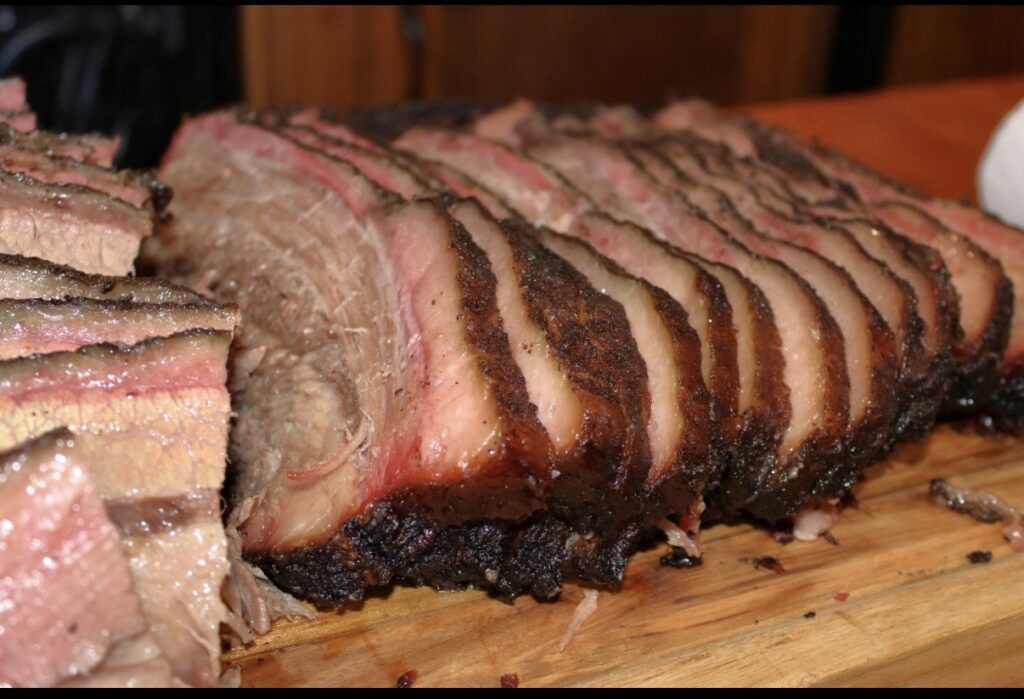 Close-up of sliced smoked brisket with a dark bark on a wooden board.